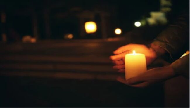 Closeup of hands holding candle with lights shining in background of darkness 