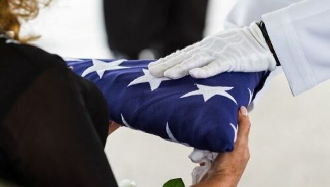 Woman accepting folded memorial US flag from white-gloved service member